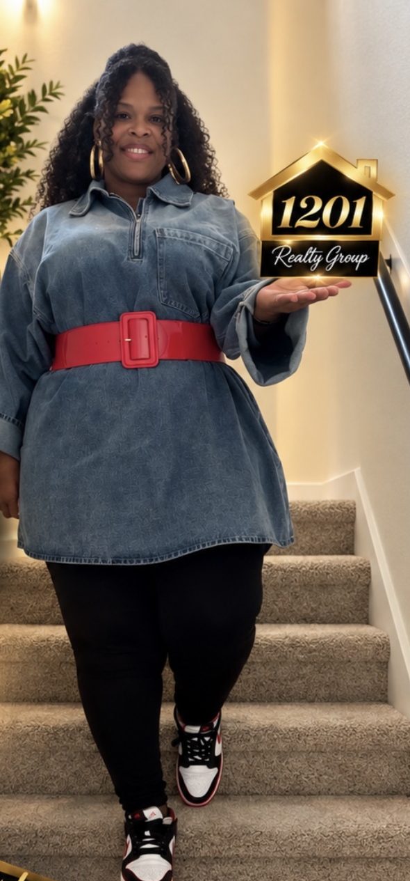 Lawanda Thornton walking down a carpeted staircase in a denim dress and red belt, holding a 1201 Realty Group sign
